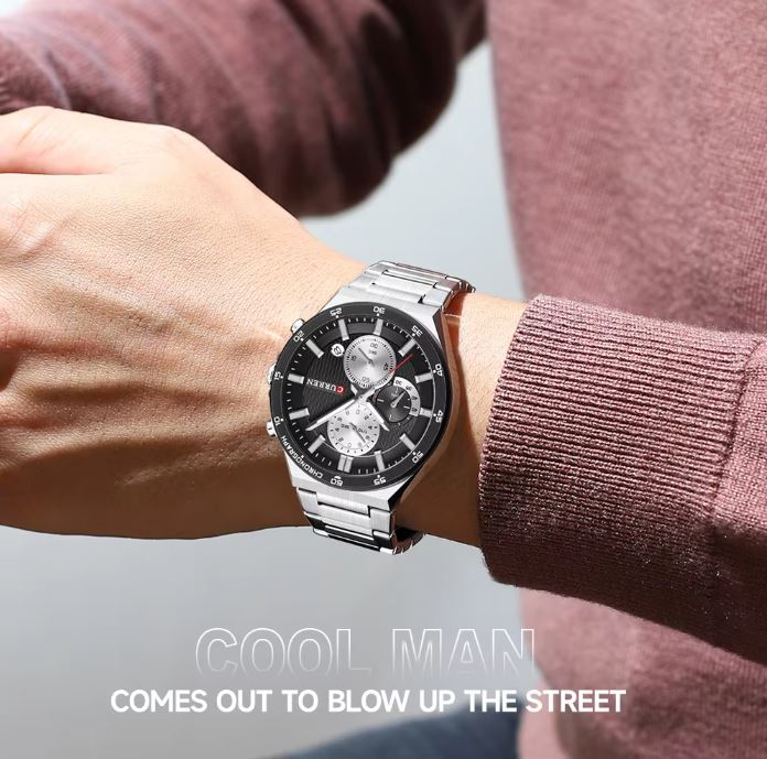 Person wearing a silver watch with a black face on a blurred background