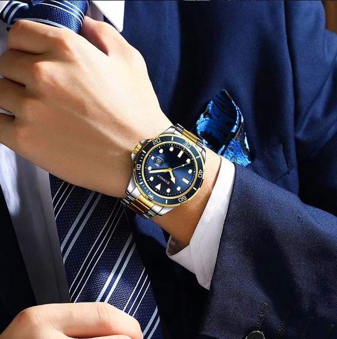 Person wearing a gold and blue wristwatch with a suit and tie in the background