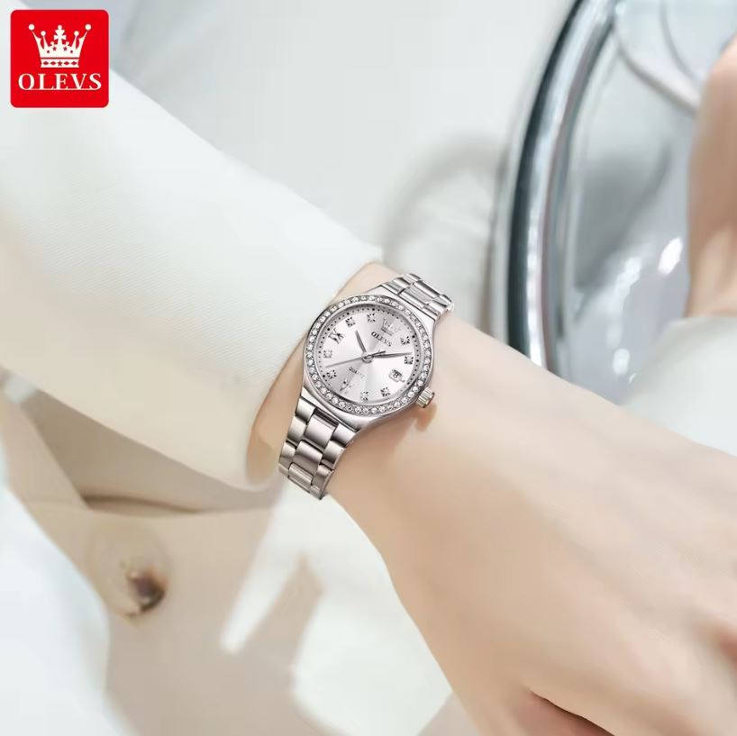 Silver wristwatch with decorative face on a wrist, brand 'OLEVS' visible