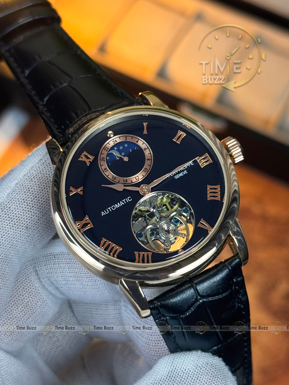 A luxury wristwatch with a dark blue dial, gold-tone case, Roman numeral hour markers, a moonphase subdial, and a visible automatic mechanical movement. The watch is held by a white-gloved hand against a warm, blurred background with a 'TIME BUZZ' watermark.