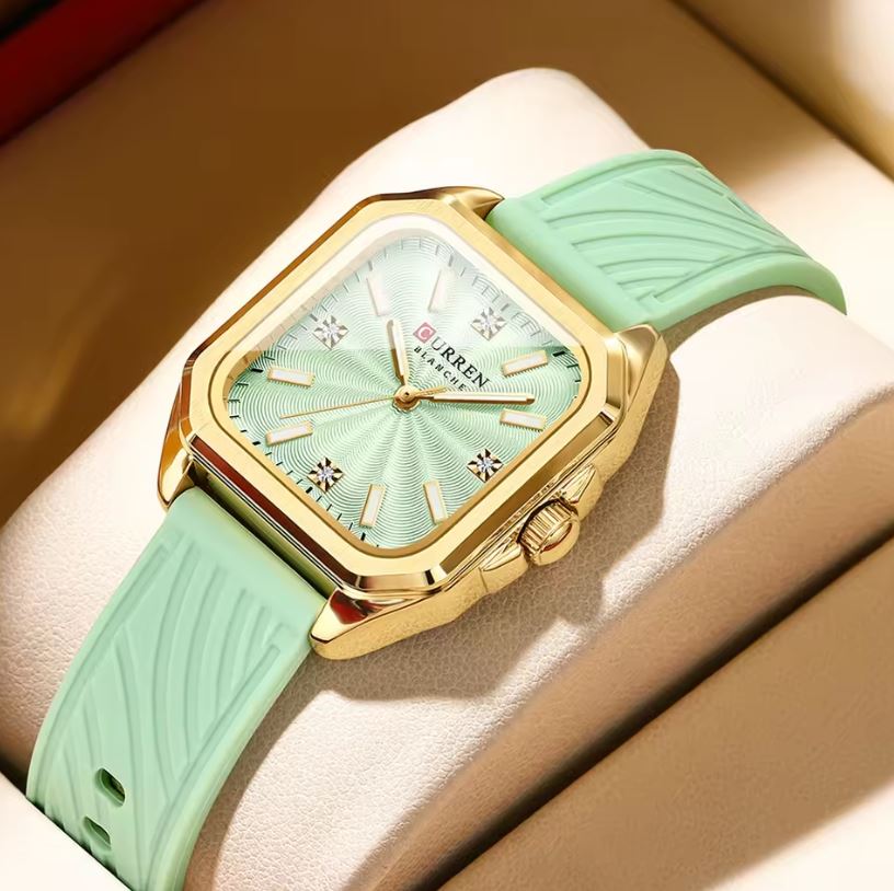 Watch with gold case and mint green strap on a beige cushion