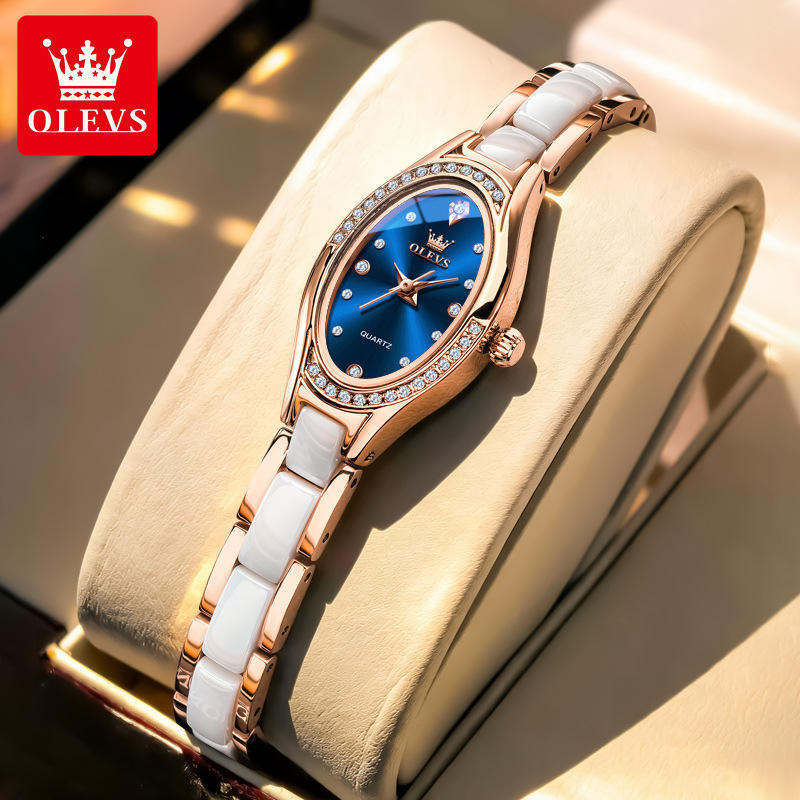 Luxury watch with rose gold and white ceramic strap on a beige cushion, brand 'OLEVS' visible.