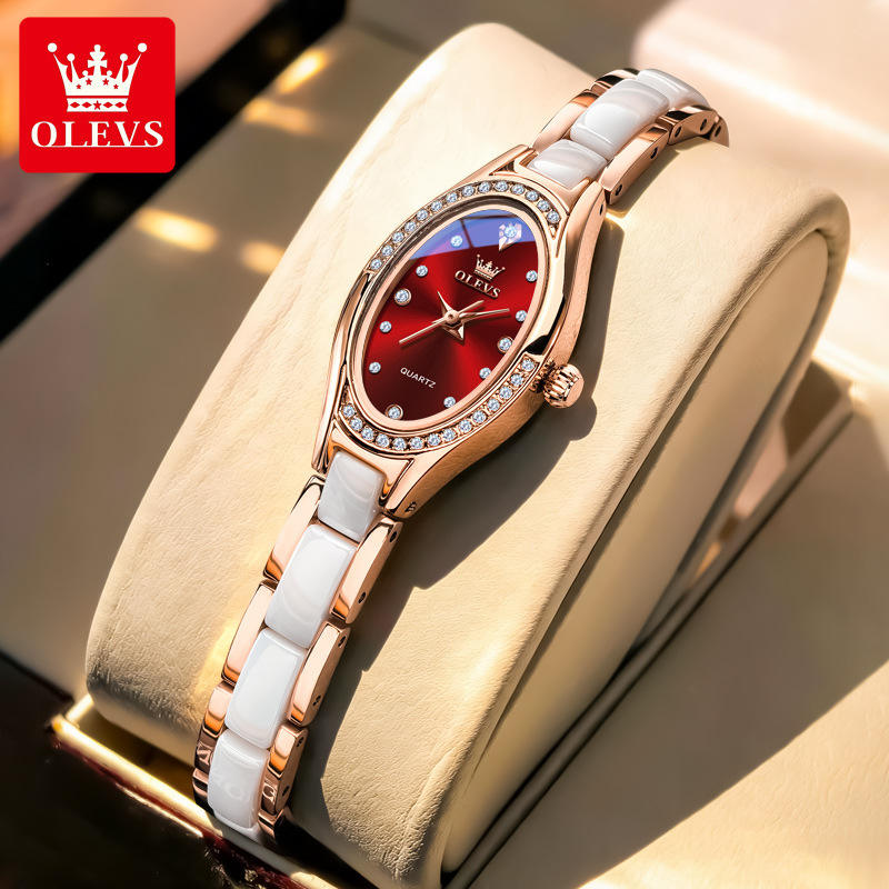 Luxury watch with red face and white strap on a beige cushion, branded OLEVS.