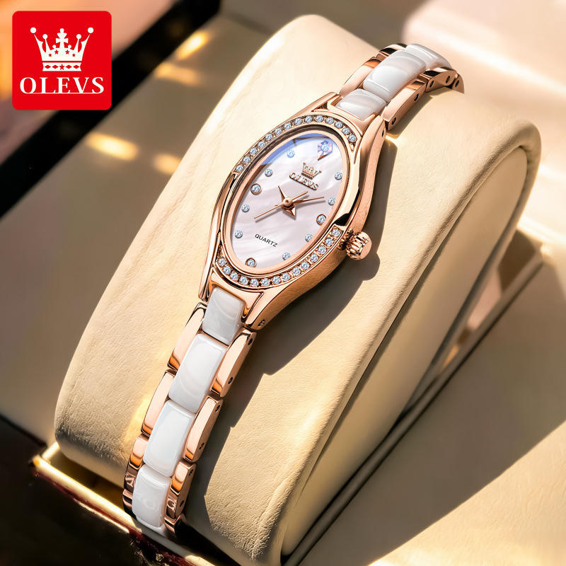 Rose gold and white ceramic watch on a beige cushion with OLEVS branding.