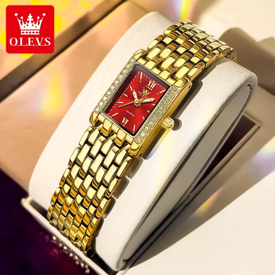 Gold watch with red face on a white cushion, brand 'OLEVS' visible