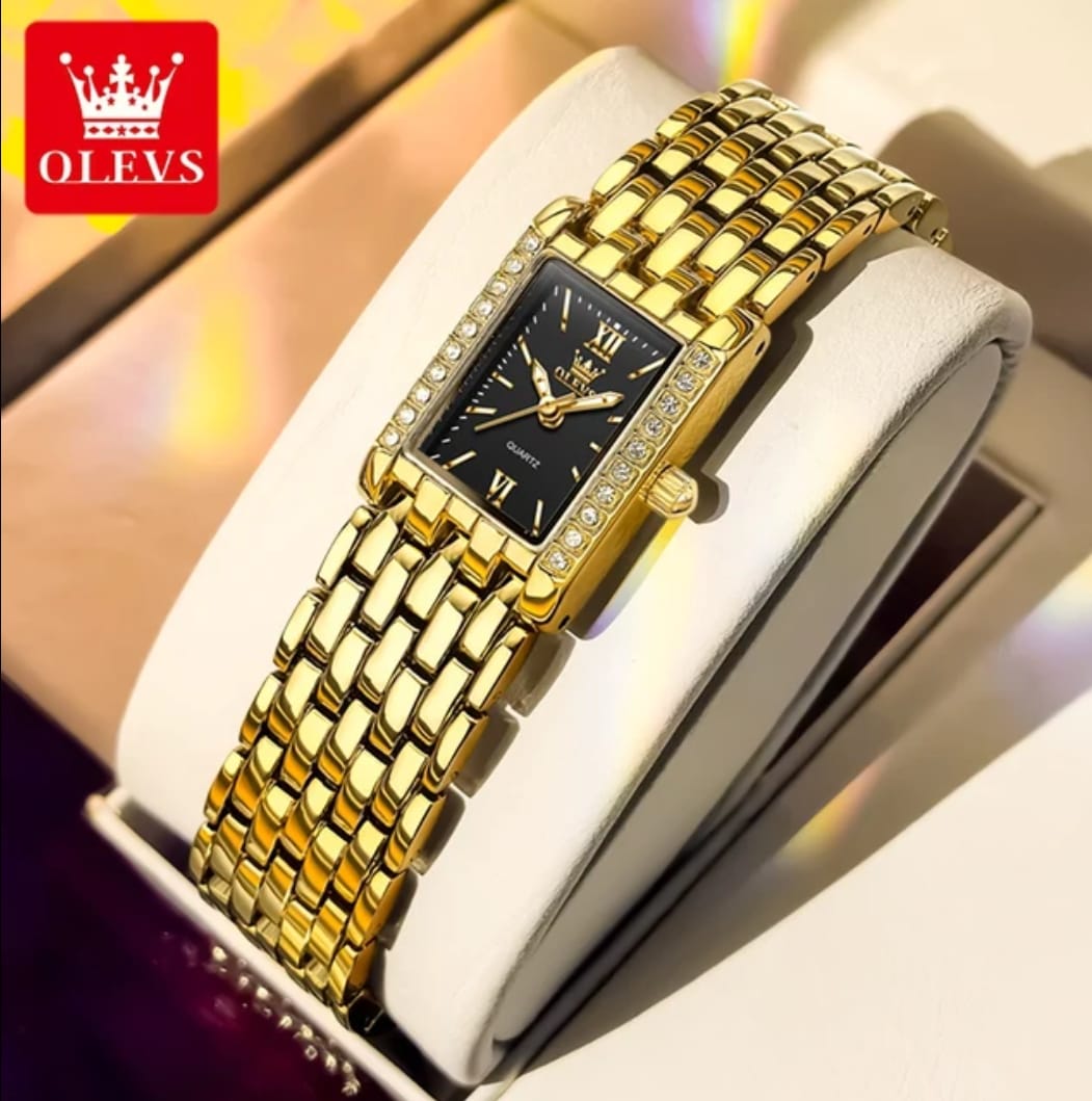Gold wristwatch with black face on a white cushion, brand 'OLEVS' visible.