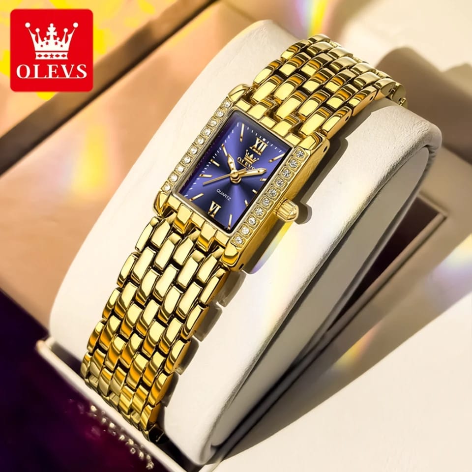 Gold wristwatch with blue face on a white cushion, brand 'OLEVS' visible.