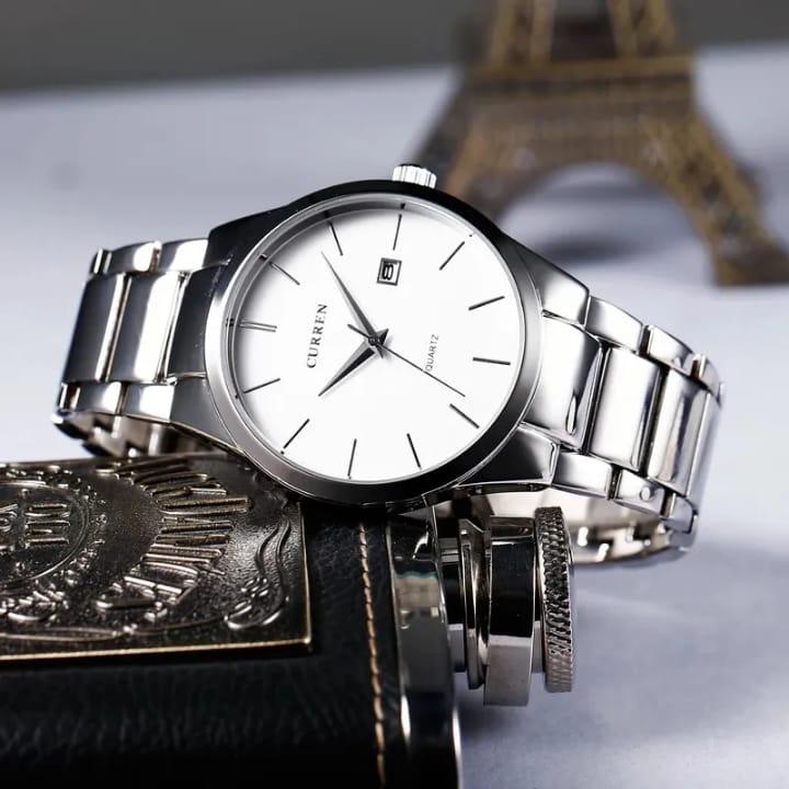 Silver wristwatch with white face on a textured surface with blurred Eiffel Tower in the background