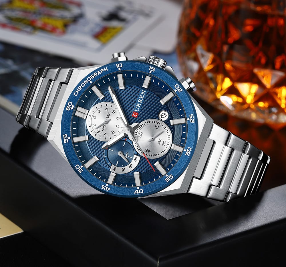 Silver and blue watch with a blurred background of cards and a glass of whiskey.