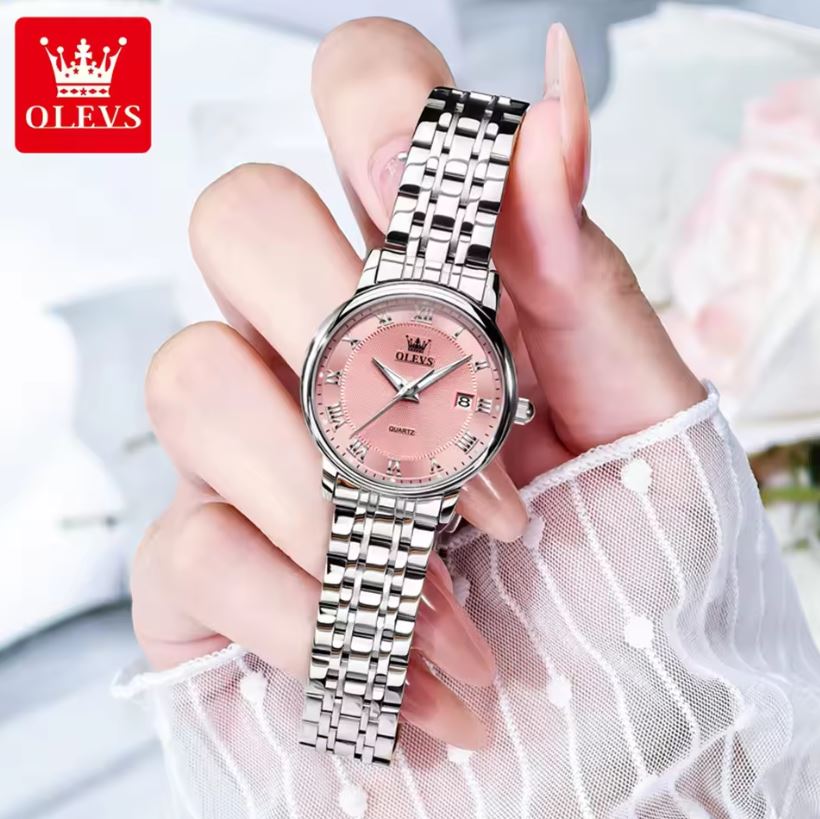Hand holding a silver watch with a pink face, brand 'OLEVS' visible.