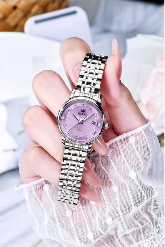 Hand holding a silver watch with a purple face against a blurred background